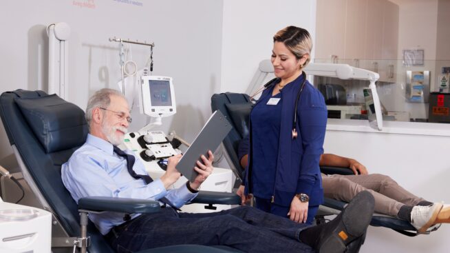 Blood donor completing paperwork in donation chair for smiling NCBB phlebotomist.