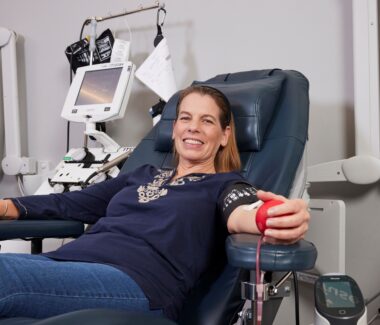 Blood donor smiling while giving blood and squeezing a foam red heart