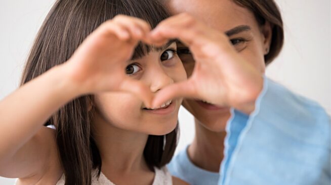 Smiling ittle girl and her mother peering through the girls heart shaped hands.